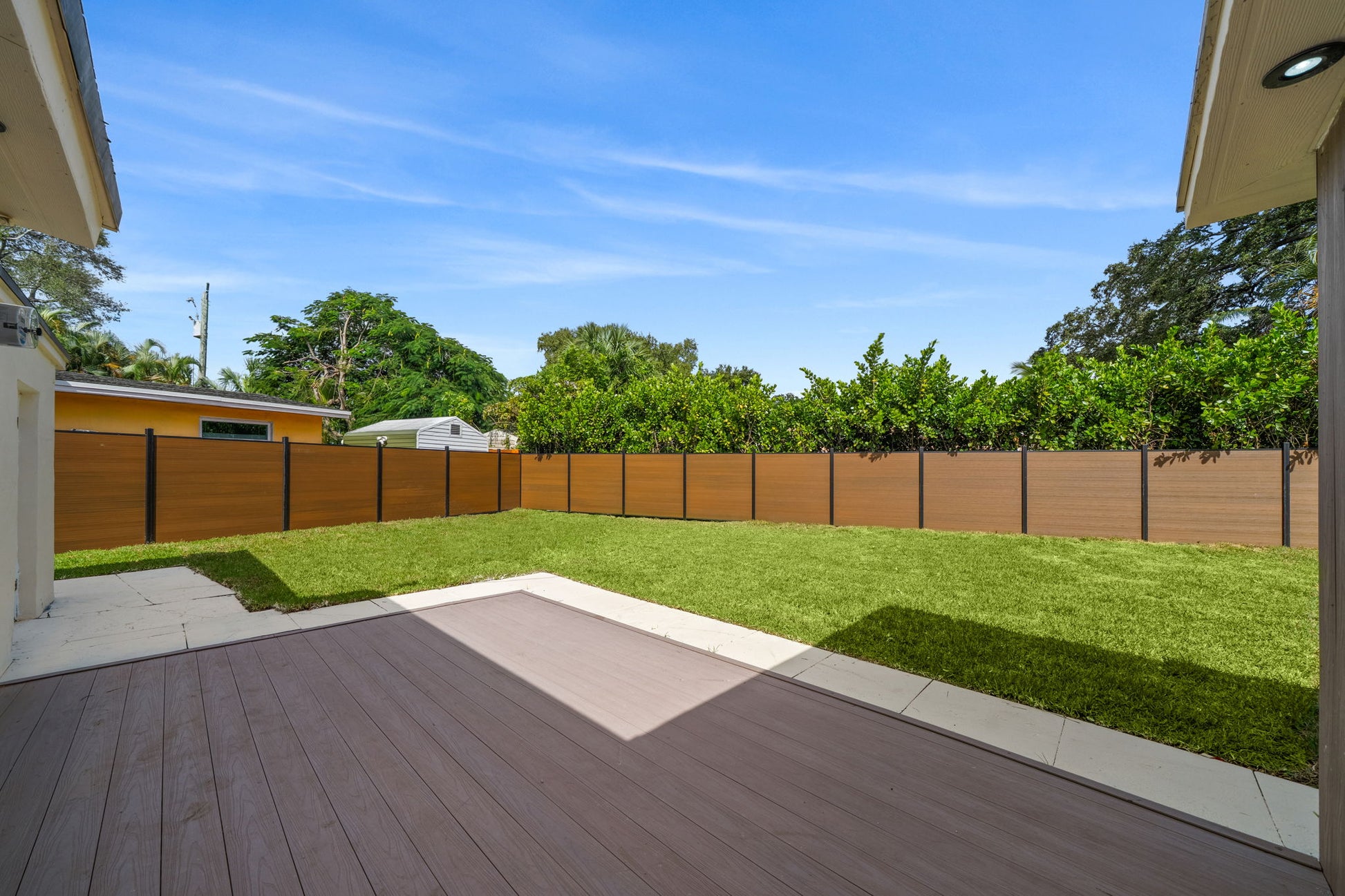 Backyard with wood-grain composite privacy fence panels and aluminum posts surrounding a modern lawn and patio area