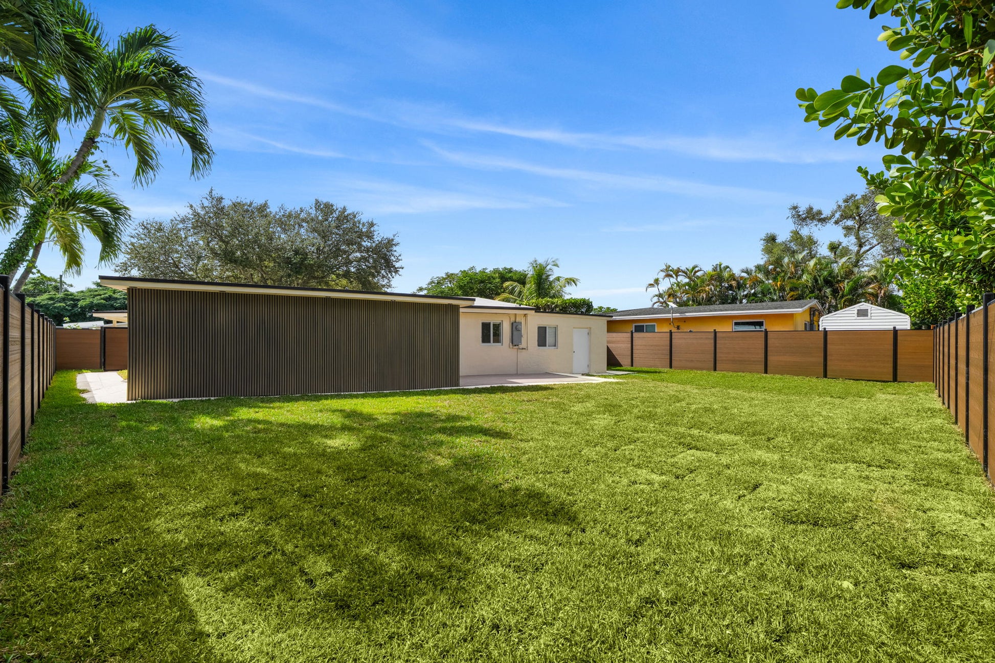 Large backyard with wood-grain composite privacy fence panels enclosing a modern residential lawn and home exterior