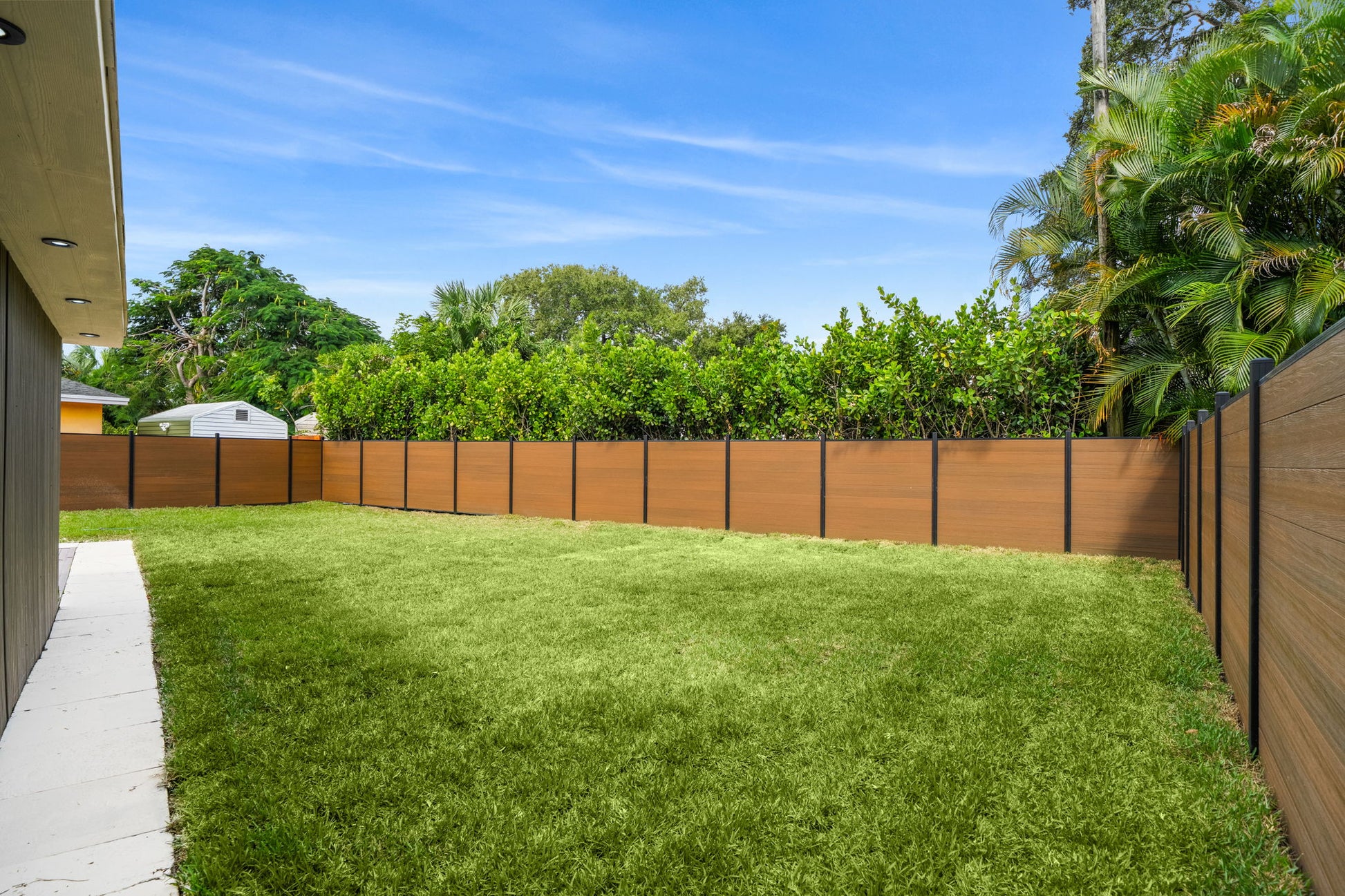 Modern backyard enclosed with wood-grain composite privacy fence panels and aluminum posts